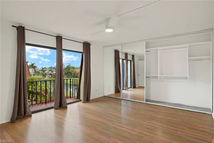 Spacious room with wood-finish flooring, a ceiling fan, and a built-in wardrobe featuring mirrored sliding doors and integrated shelving