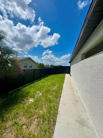 Exterior side yard featuring a concrete walkway, green lawn, and dark perimeter fencing