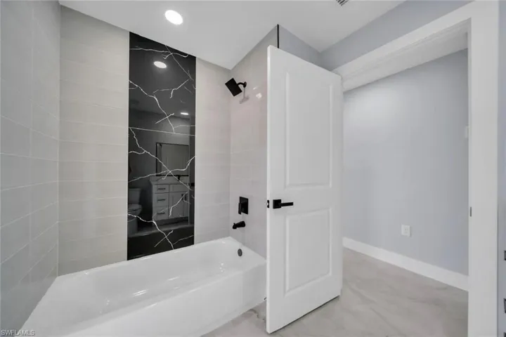 Bathtub with matte black fixtures and a striking black and white patterned accent tile wall