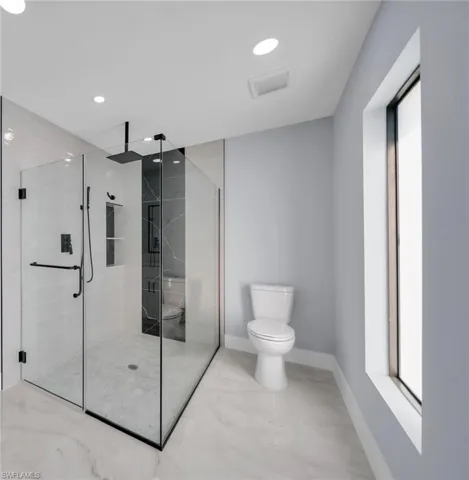 Spacious bathroom featuring a glass-enclosed shower with matte black fixtures, integrated shelving, and large format white tile flooring