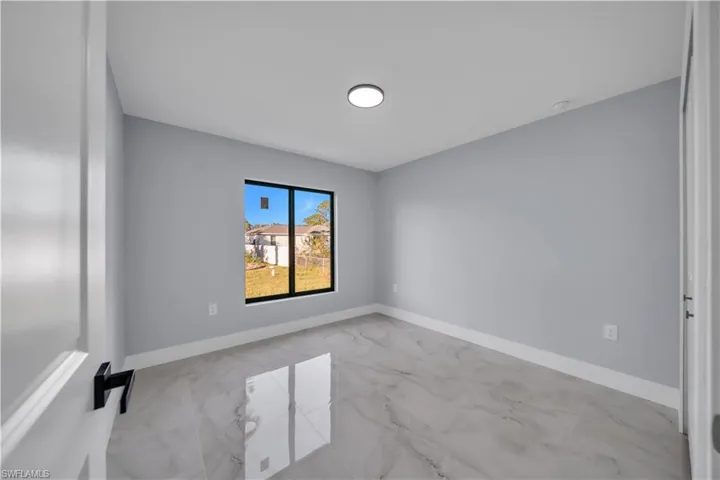 Room featuring a window with black trim, white baseboards, a flush-mount ceiling light, and polished marble-look flooring