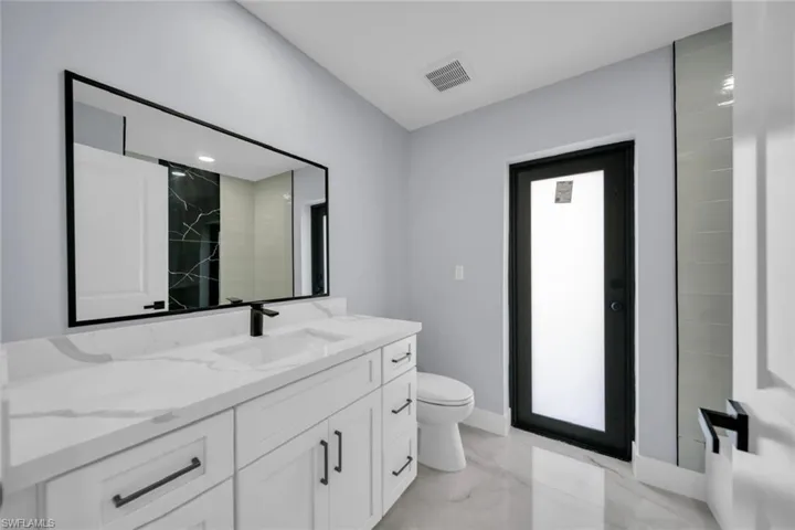Contemporary bathroom featuring a white vanity with integrated sink, a large framed mirror, and a black-framed opaque glass door