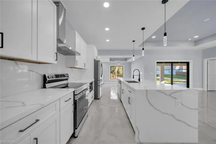 Kitchen featuring white cabinetry, quartz countertops, stainless steel appliances, a large island with an undermount sink and a matte black faucet, and recessed and pendant lighting