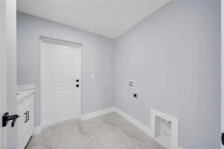 Utility room featuring light gray walls, white baseboards, and marble-look tile flooring
