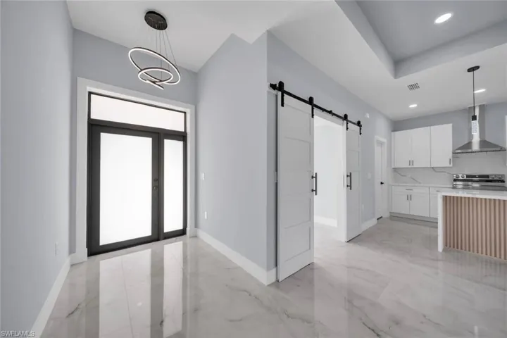 Foyer featuring a modern chandelier, double entry doors with transom window, and large format marble-look tile flooring