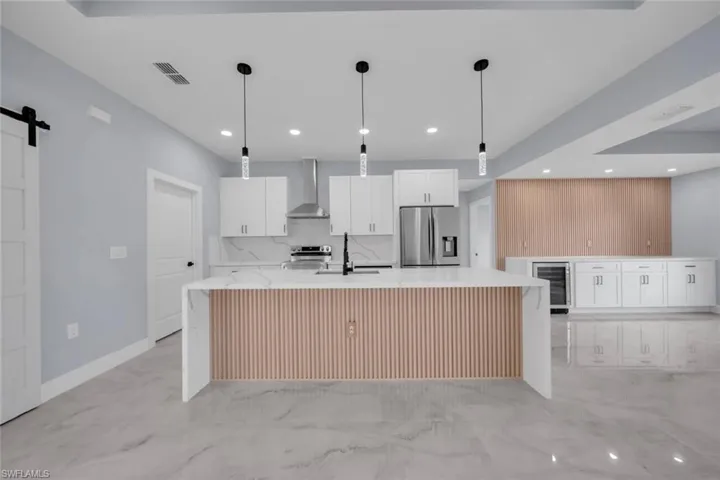 Spacious kitchen featuring an oversized island with slat wood-finish paneling, white shaker cabinetry, stainless steel appliances, and quartz countertops with a matching backsplash
