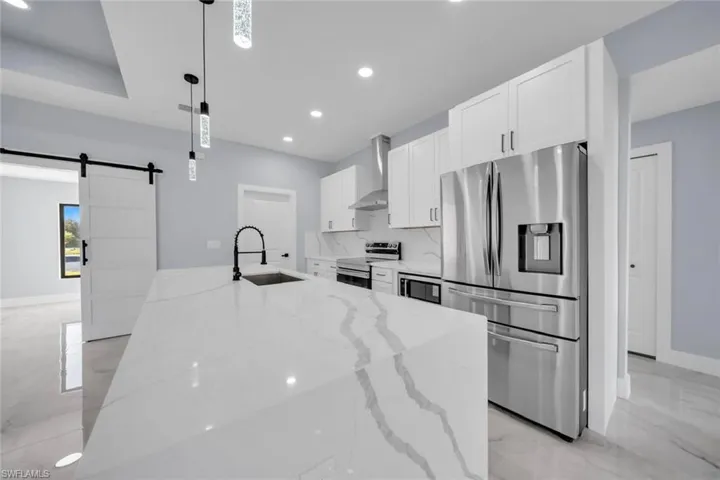 Spacious kitchen featuring an extended island with a black gooseneck faucet, white shaker cabinetry, stainless steel appliances, and a white subway tile backsplash