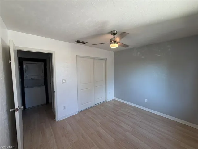 Unfurnished bedroom with stacked washer / drying machine, light wood-type flooring, a closet, ceiling fan, and a textured ceiling