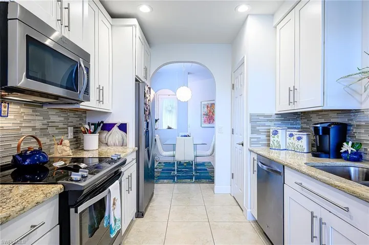 Kitchen with stainless steel finishes, tasteful backsplash, light stone counters, and white cabinetry