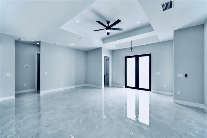 Unfurnished room with a raised ceiling, french doors, ceiling fan, light marble finish floors, and recessed lighting