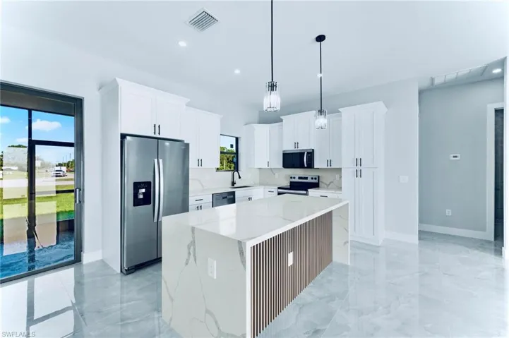 Kitchen featuring appliances with stainless steel finishes, white cabinetry, a center island, light marble finish flooring, and recessed lighting