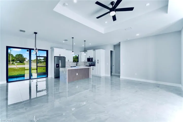 Kitchen with a raised ceiling, open floor plan, white cabinetry, an island with sink, and stainless steel appliances
