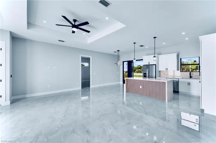 Kitchen with a kitchen island, white cabinets, open floor plan, a tray ceiling, and decorative light fixtures