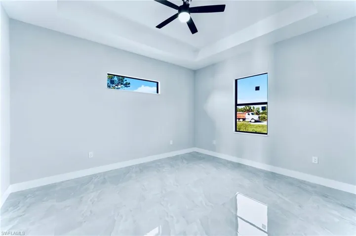 Unfurnished room with a raised ceiling, healthy amount of natural light, and a ceiling fan