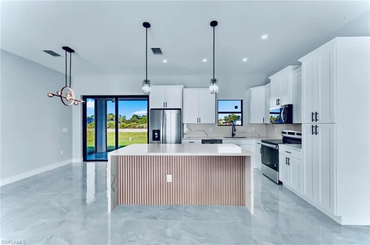 Kitchen with a center island, light marble finish floors, stainless steel appliances, pendant lighting, and healthy amount of natural light