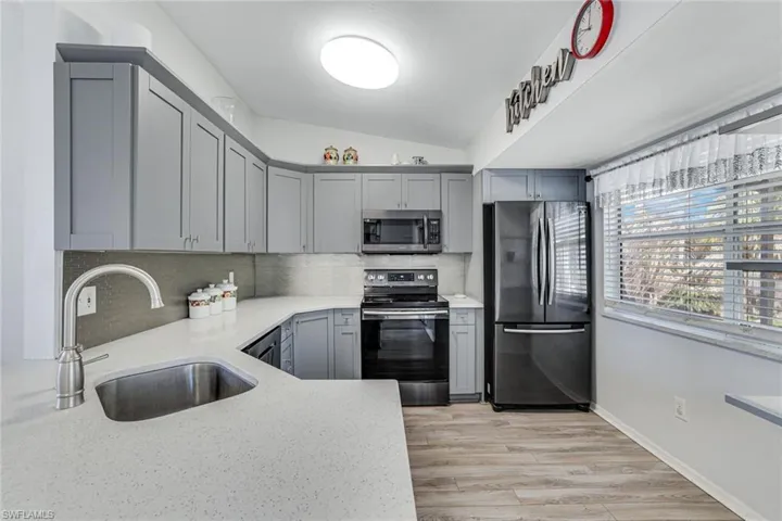 Kitchen with light stone countertops, decorative backsplash, stainless steel appliances, gray cabinetry, and lofted ceiling
