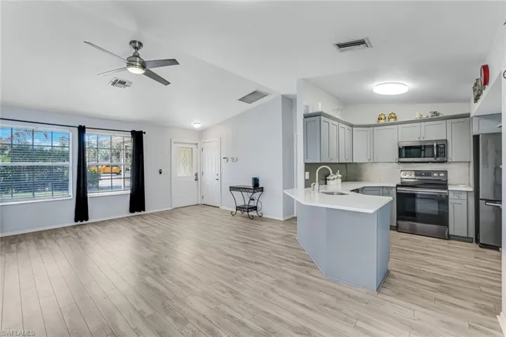 Kitchen featuring lofted ceiling, stainless steel appliances, gray cabinets, backsplash, and a peninsula