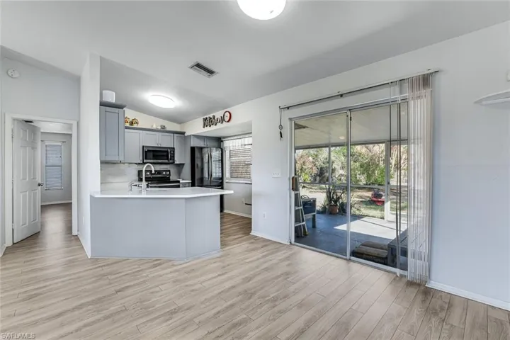 Kitchen with gray cabinetry, vaulted ceiling, stainless steel appliances, a peninsula, and light wood-style flooring
