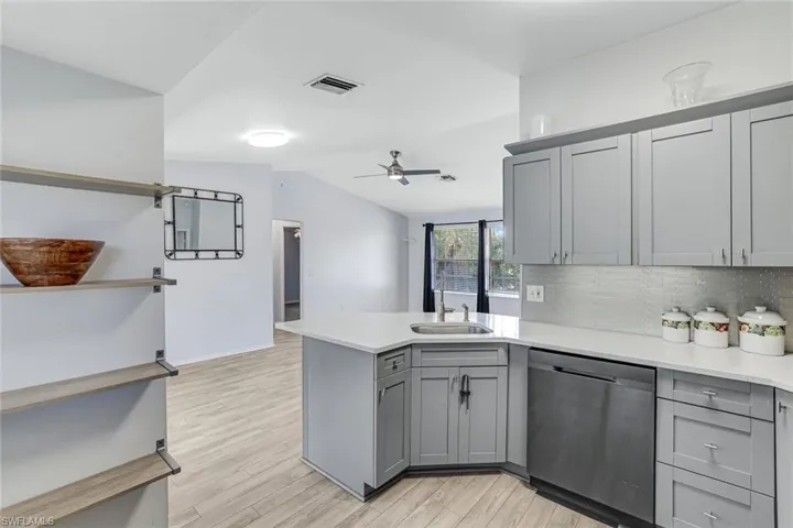 Kitchen featuring gray cabinetry, a peninsula, stainless steel dishwasher, backsplash, and lofted ceiling