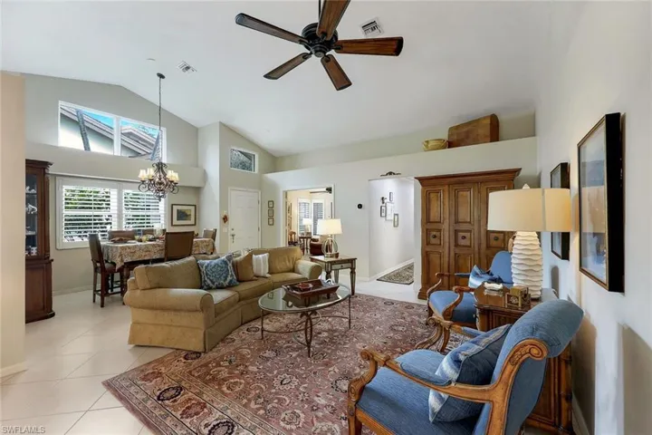 Living room with light tile patterned floors, ceiling fan with notable chandelier, and high vaulted ceiling