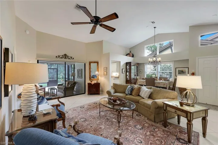 Tiled living room with ceiling fan with notable chandelier and high vaulted ceiling