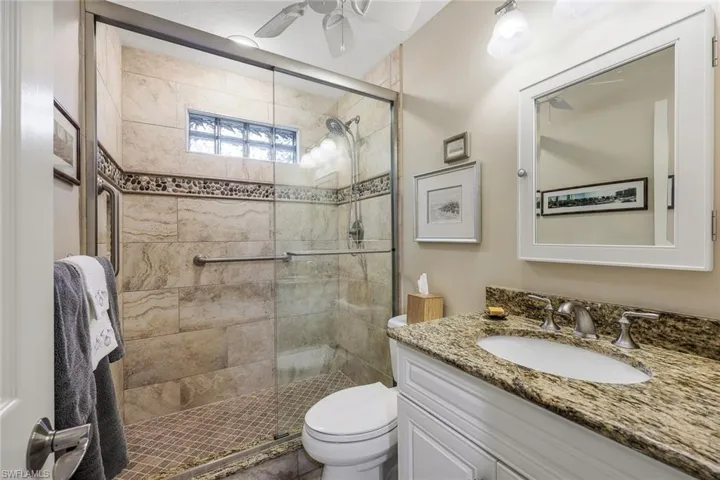 Bathroom featuring ceiling fan, vanity, a shower with shower door, and toilet