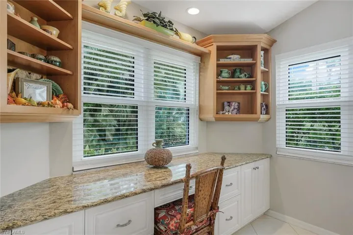 Kitchen featuring light stone counters, built in desk, white cabinets, and light tile patterned flooring