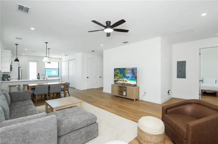 Living room with recessed lighting, light wood finished floors, electric panel, and a ceiling fan - Virtually Edited Image