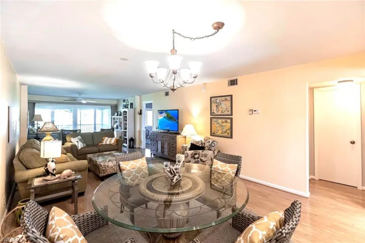 Open living / dining area with sweeping views of the golf course to 18th hole, light wood-style flooring,  chandelier and ceiling fan