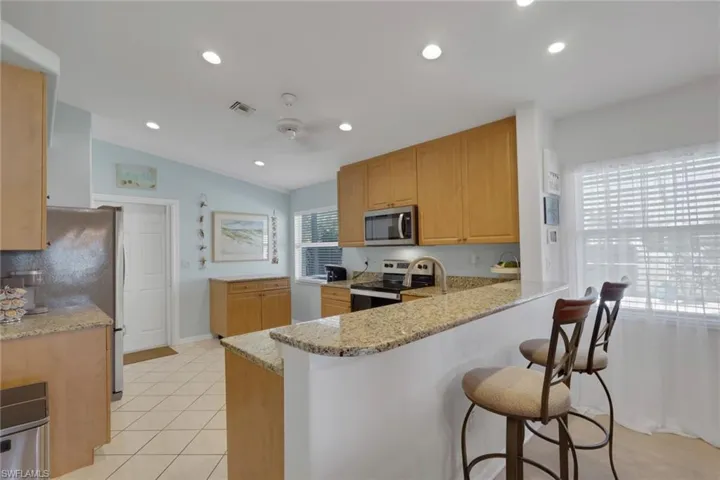 Kitchen with light stone countertops, a peninsula, stainless steel appliances, vaulted ceiling, and recessed lighting