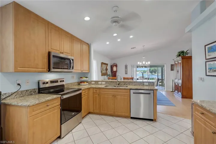 Kitchen featuring stainless steel appliances, light stone counters, a peninsula, lofted ceiling, and hanging lights