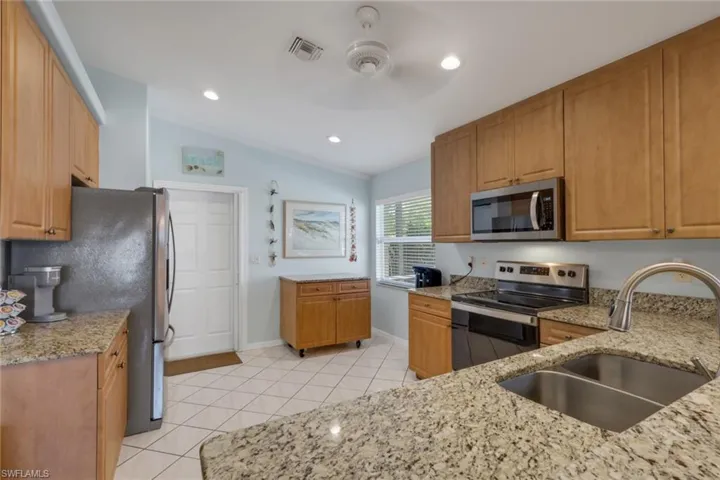 Kitchen with stainless steel appliances, light stone countertops, lofted ceiling, a ceiling fan, and light tile patterned floors