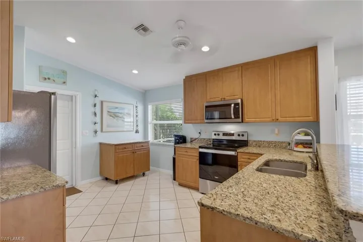 Kitchen with light stone countertops, stainless steel appliances, wood finish cabinets, ceiling fan, and light tile patterned flooring