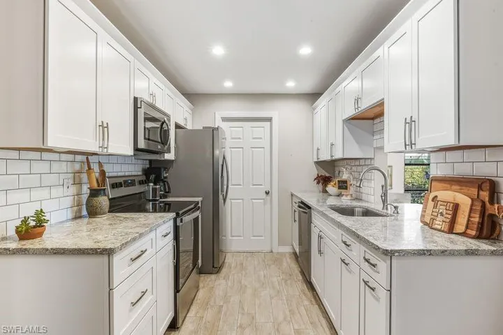 Updated kitchen with tiled flooring, stainless steel appliances, beautiful quartz countertops, modern white cabinets, tasteful tile backsplash, and recessed lighting.