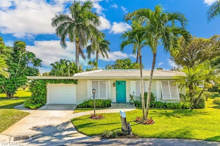 Front view of the home with a concrete driveway, tiled roof, beautifully landscaped yard with mature plantings, Bahama style window coverings, and a one car attached garage.