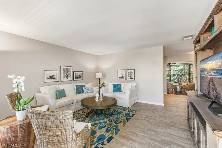 Living room with tiled wood-look floors looking into the kitchen/sunroom area.