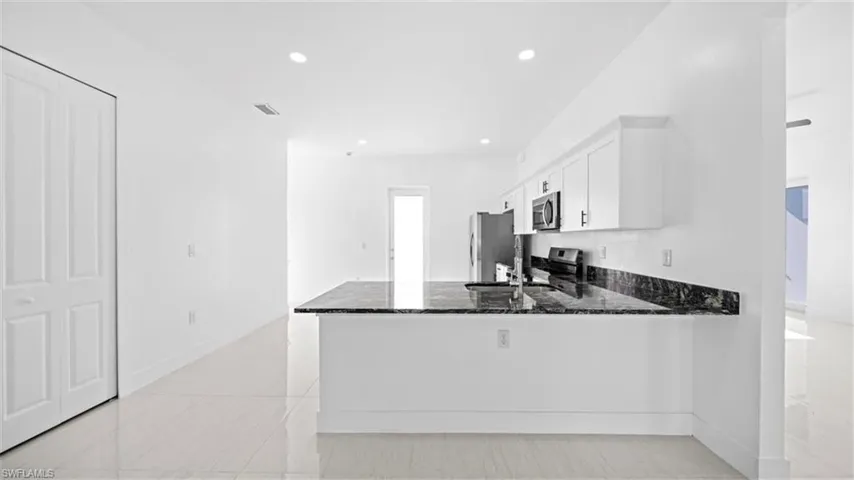 Kitchen featuring dark stone countertops, white cabinetry, a peninsula, recessed lighting, and stainless steel appliances