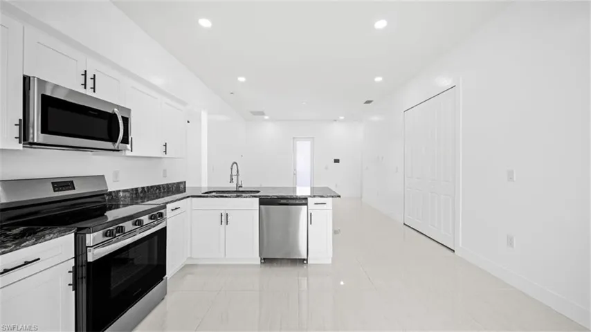 Kitchen with stainless steel appliances, dark stone counters, a peninsula, recessed lighting, and white cabinets