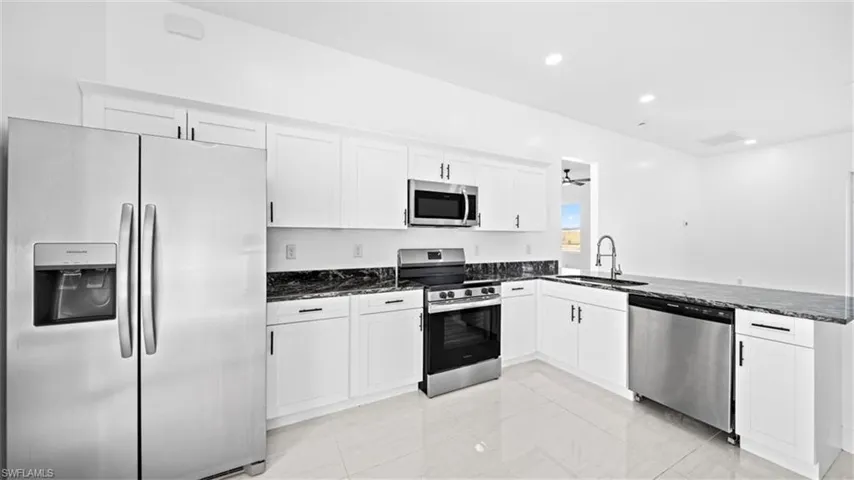 Kitchen with stainless steel appliances, white cabinets, dark stone counters, recessed lighting, and a peninsula