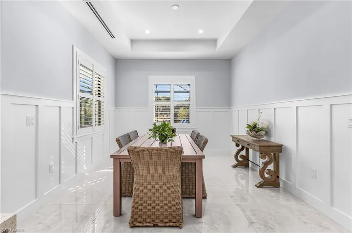 Dining space with a tray ceiling, light marble finish floors, a wainscoted wall, and recessed lighting