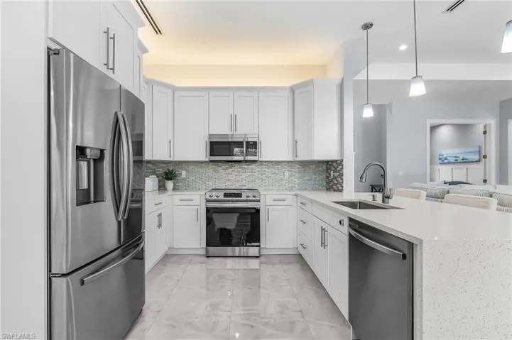 Kitchen featuring appliances with stainless steel finishes, light stone counters, white cabinets, a peninsula, and recessed lighting