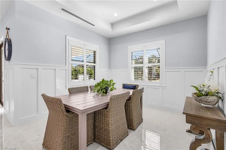 Dining space with a decorative wall, wainscoting, a tray ceiling, recessed lighting, and light tile patterned flooring