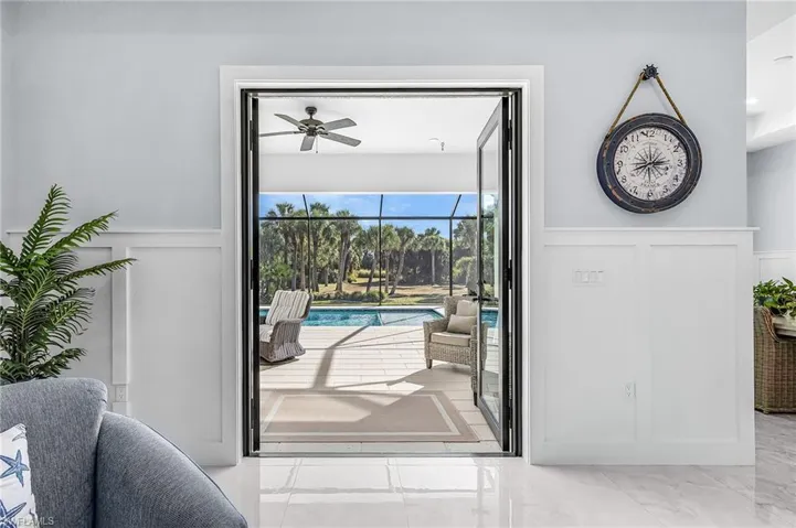 Doorway to outside featuring a decorative wall, wainscoting, a sunroom, marble look tile flooring, and ceiling fan
