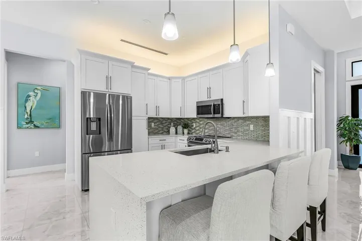 Kitchen with stainless steel appliances, a peninsula, light stone counters, a kitchen breakfast bar, and light marble finish floors