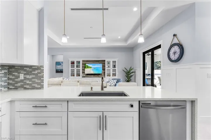 Kitchen featuring light stone countertops, dishwasher, tasteful backsplash, a tray ceiling, and pendant lighting
