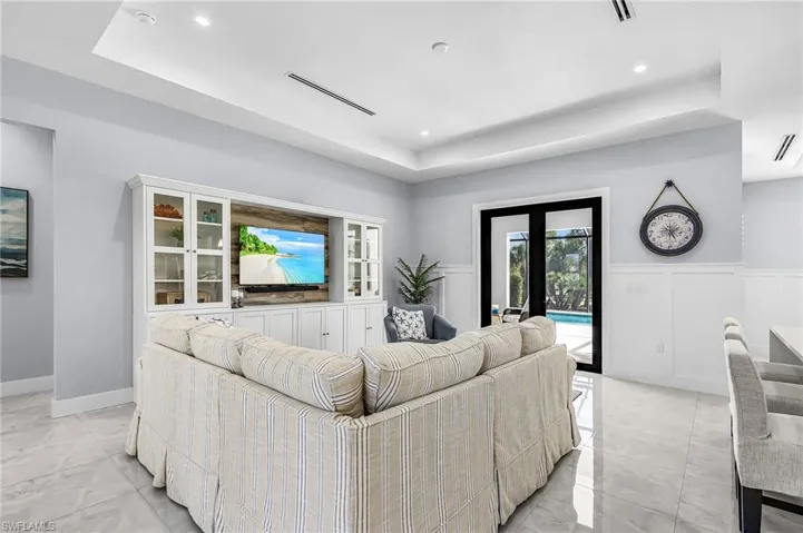 Living area with french doors, a raised ceiling, recessed lighting, and wainscoting