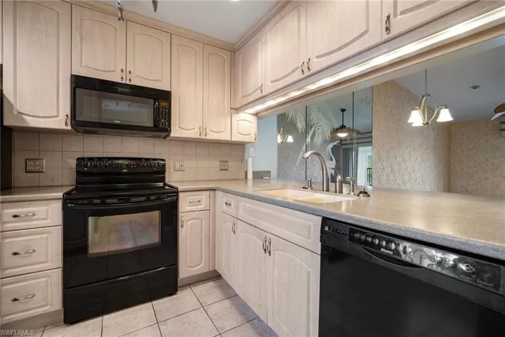 Kitchen featuring hanging light fixtures, black appliances, sink, tasteful backsplash, and light tile patterned floors
