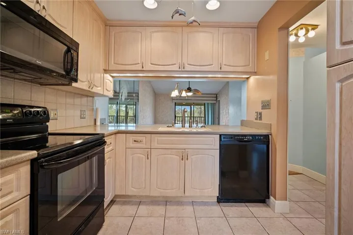 Kitchen with black appliances, sink, tasteful backsplash, light tile patterned floors, and light brown cabinetry
