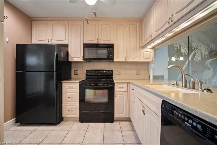 Kitchen with black appliances, light brown cabinets, sink, and light tile patterned floors
