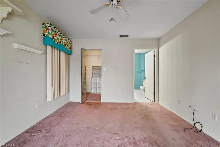 Unfurnished bedroom with ensuite bathroom, carpet flooring, and ceiling fan